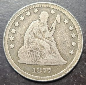 Silver coin with a seated liberty design and '1877' on a dark background