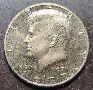 U.S. half dollar with Kennedy's profile and 'In God We Trust' inscription.
